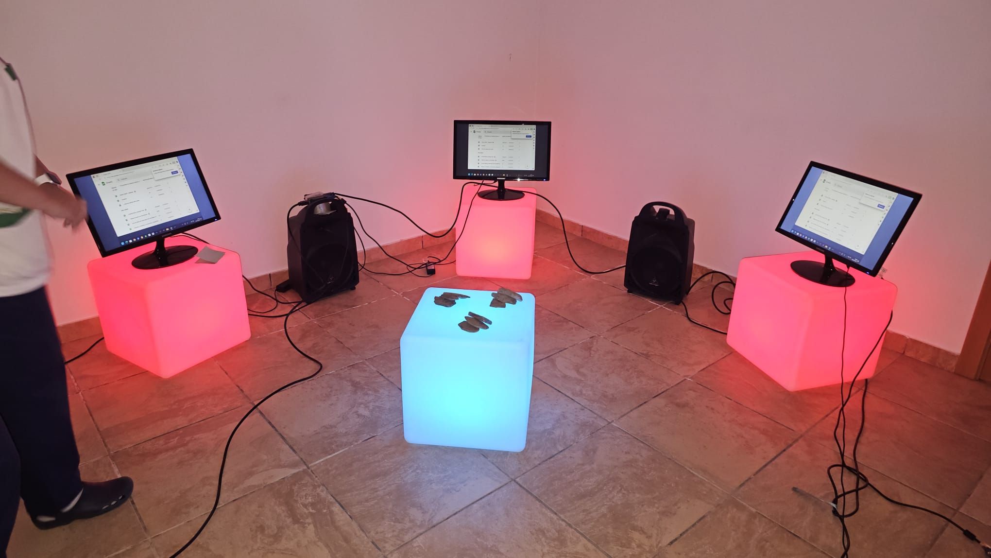 Montagem de Pedras que Gritam, com três monitores sobre cubos vermelhos e pedras sobre um cubo azul
